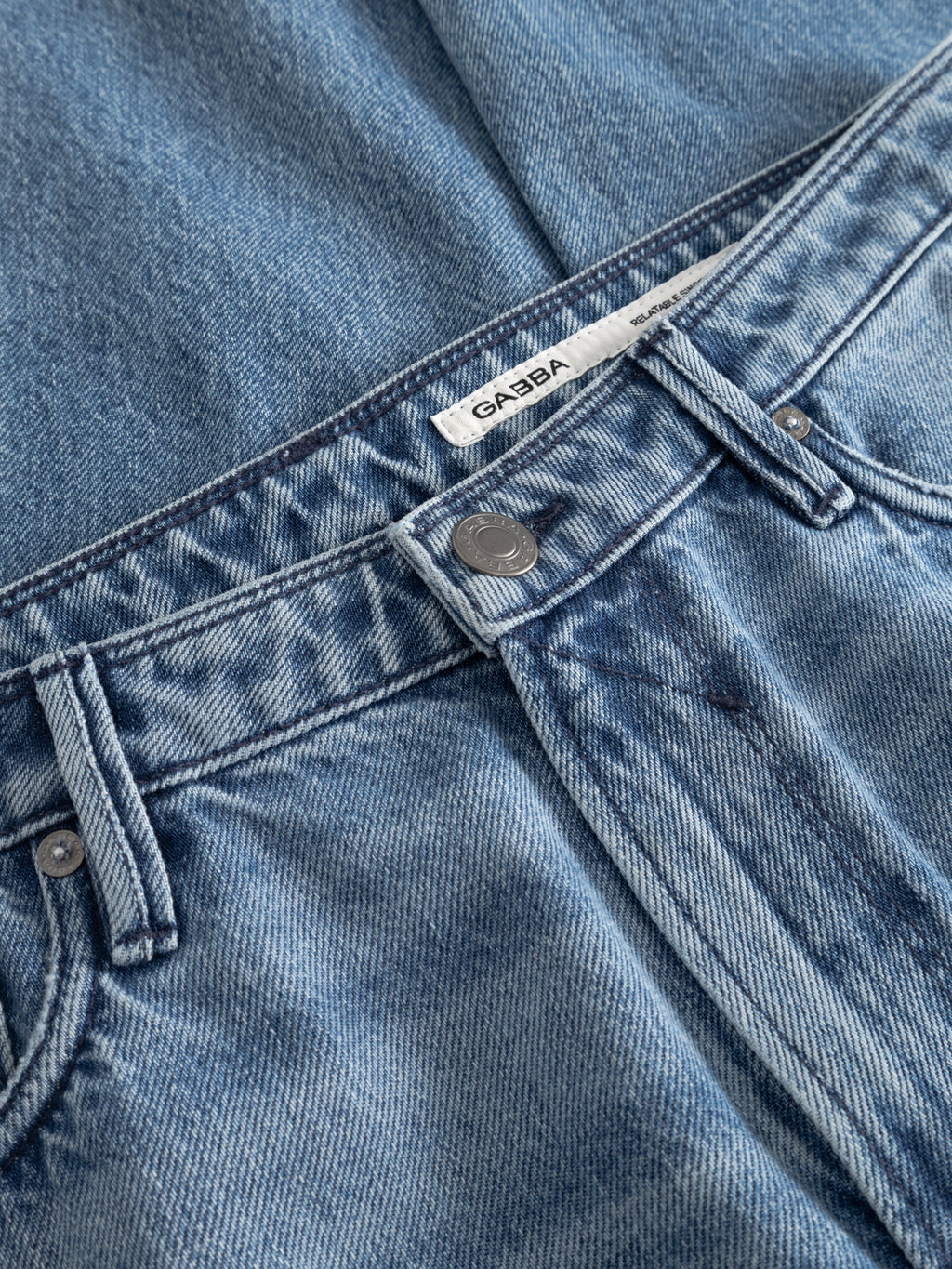 Close-up of Gabba GABmax Elvis Jeans in mid blue denim with a relaxed fit, metal button, belt loops, white inner waistband label, classic stitching, and front pocket.