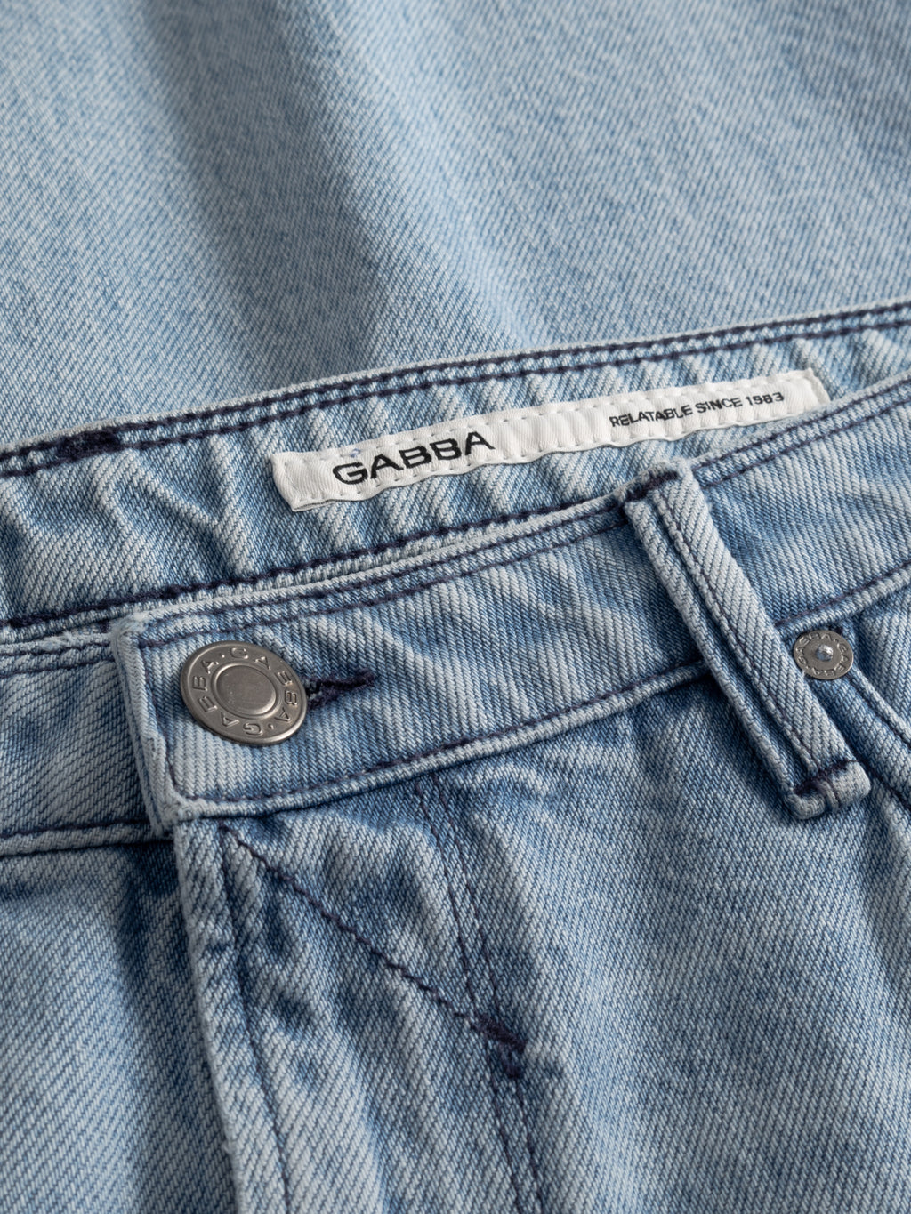 Close-up of Gabba GABmax Elvis Jeans in light blue denim featuring a metal button, belt loops, front seam, and a white label with the Gabba brand above the waistband.