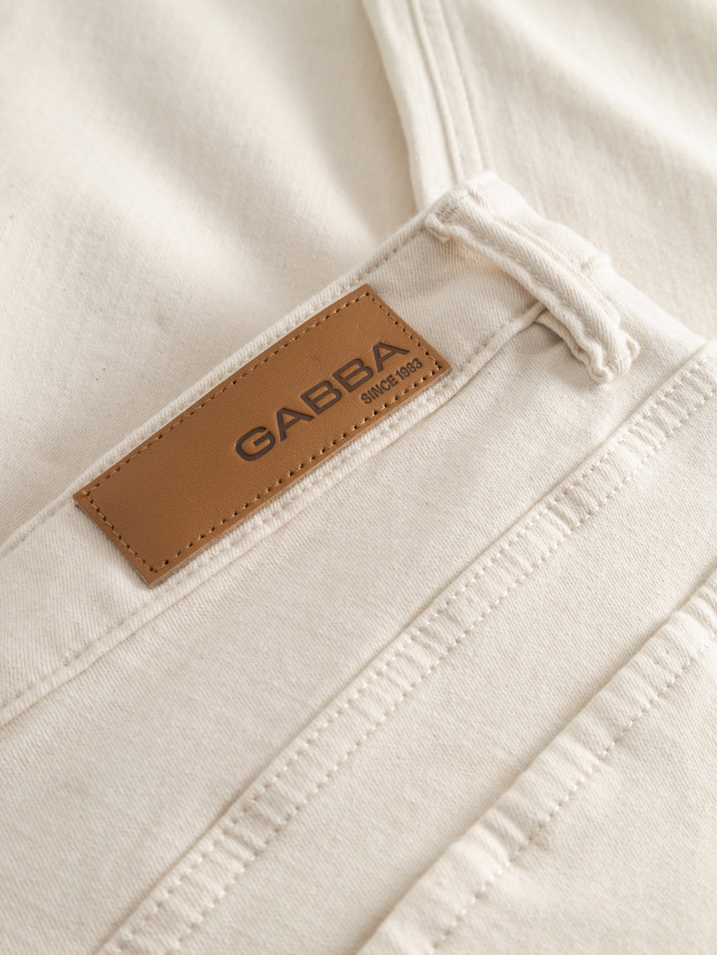 Close-up of cream-colored GABjones Heski Jeans - Ecru by Gabba, showcasing a brown leather patch with the brand name and 