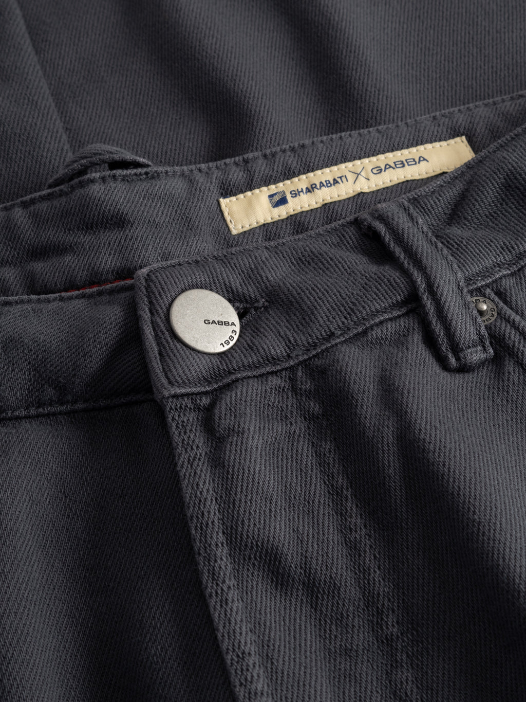 Close-up of GABcarl Blancel TENCEL™ Jeans - Black by Gabba, featuring dark grey denim in a TENCEL cotton blend, a metal Gabba button at the waistband, and a beige Shahabati x Gabba label.
