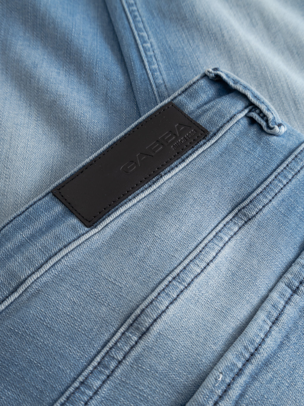 Close-up of GABjones Mik Jeans in light blue denim by Gabba, highlighting detailed stitching and a black leather patch embossed with the brand name.