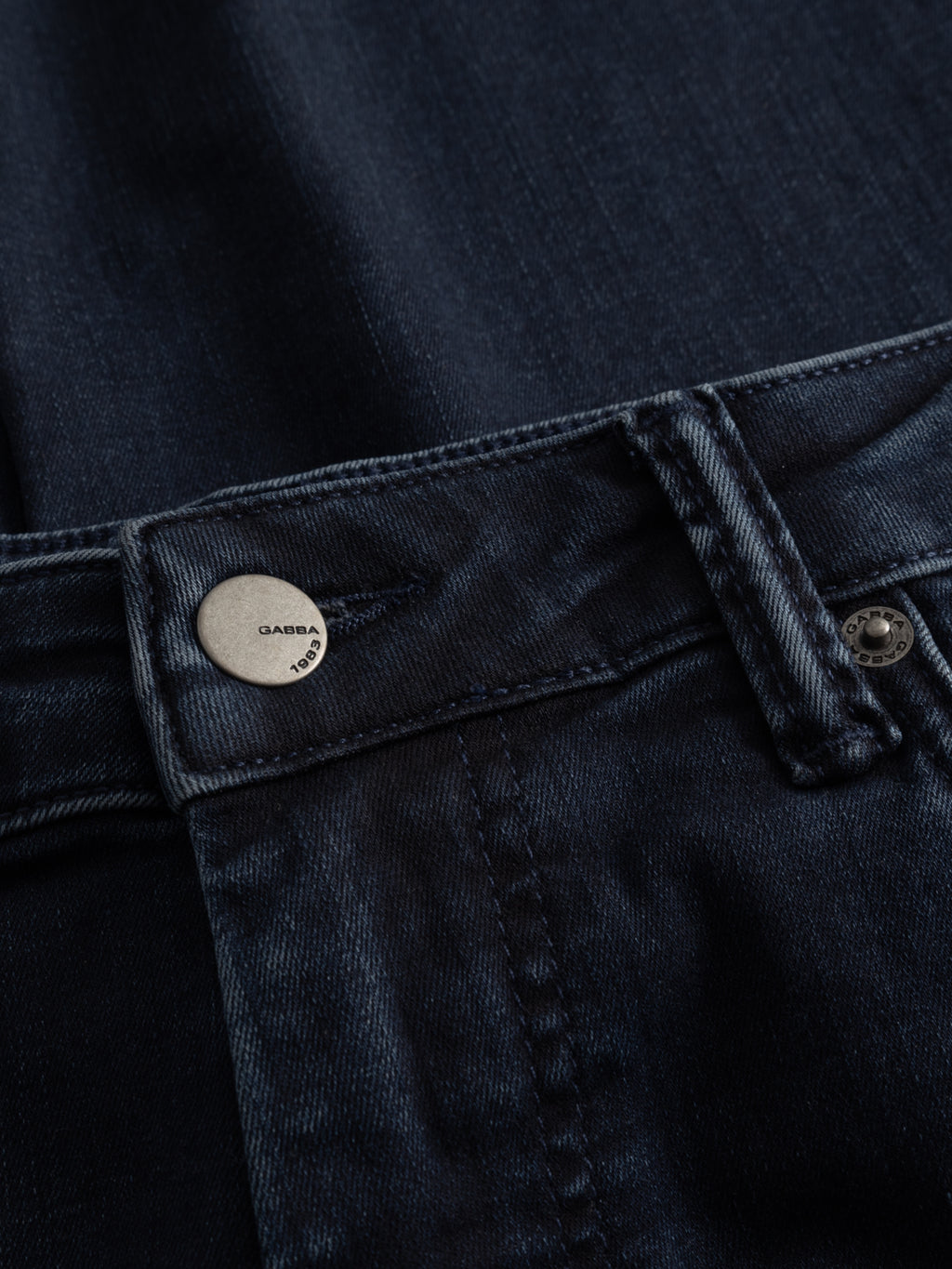 Close-up of Gabba GABjones Blueblack Jeans in blue-black denim, highlighting the waistband, belt loop, metallic Gabba 1983 button, and detailed stitching. Features a slim straight fit engineered for all-day comfort and flexibility.