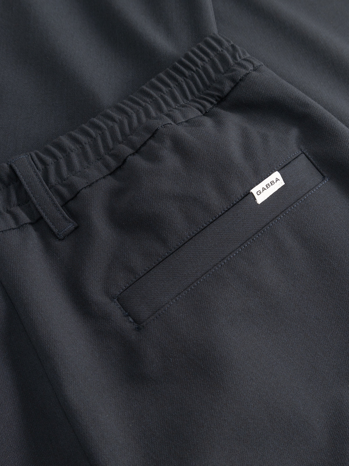 Close-up of the back pocket area of the GABnapoli 19 Phin GRS - Blue Black wool blend chinos by Gabba, featuring an elastic waistband and a small white tag near the pocket. These pants offer a regular straight fit.
