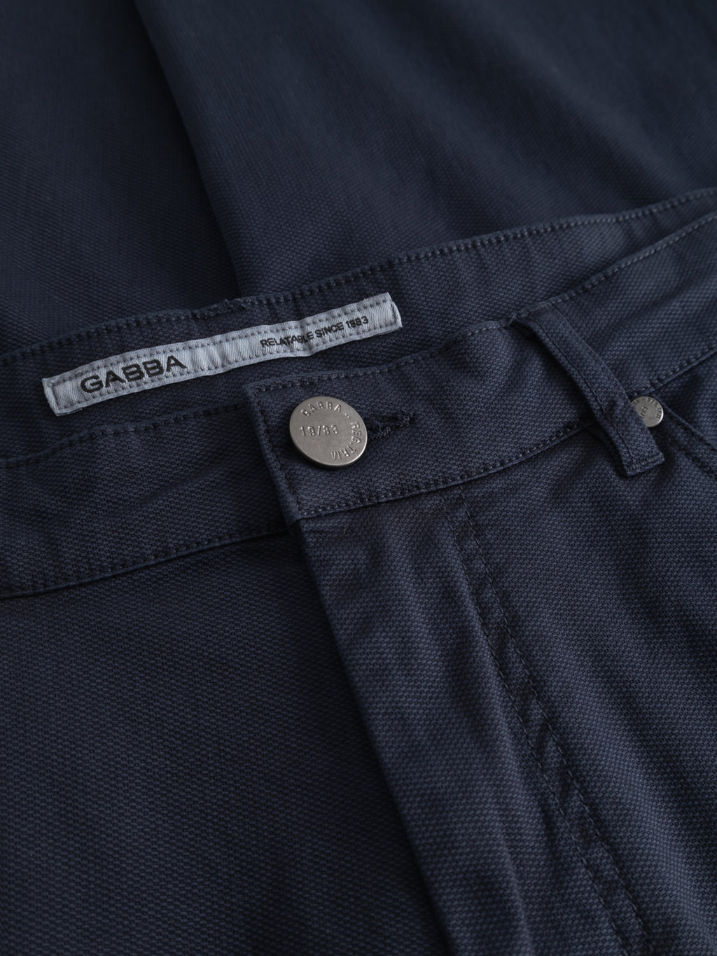 Close-up of dark navy GABmarc 5poc Marlo jeans by Gabba, featuring a metal button engraved with Gabba Jeans and a white label on the waistband reading 