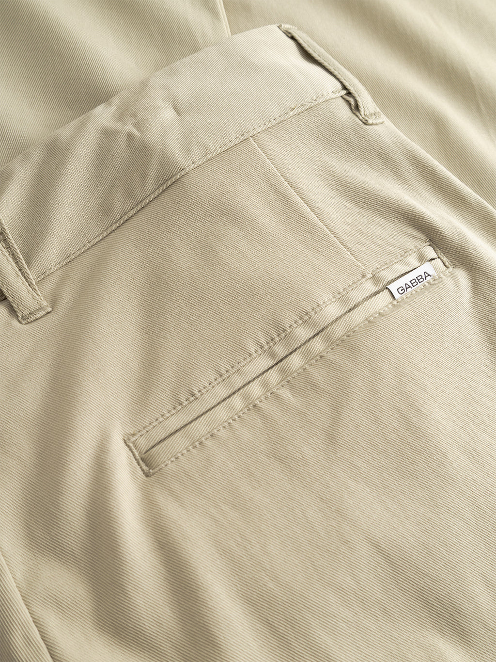 Close-up of the back pocket of Gabba's GABfirenze Bolu Cropped TENCEL™ Pant in Alfa Green, featuring a small white Gabba label by the pocket opening. The stretch twill fabric has a smooth, subtly textured look.