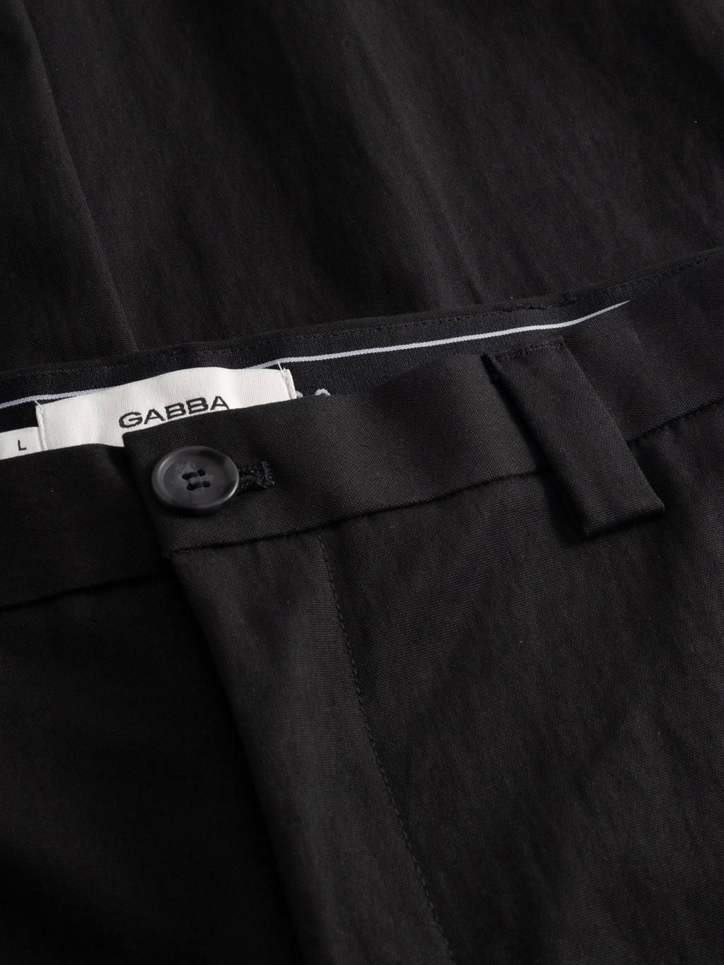 Close-up of the waistband on the GABdenver Fuggies Pant - Black by Gabba, featuring a black button, belt loop, and part of the inside label with brand name and size L.