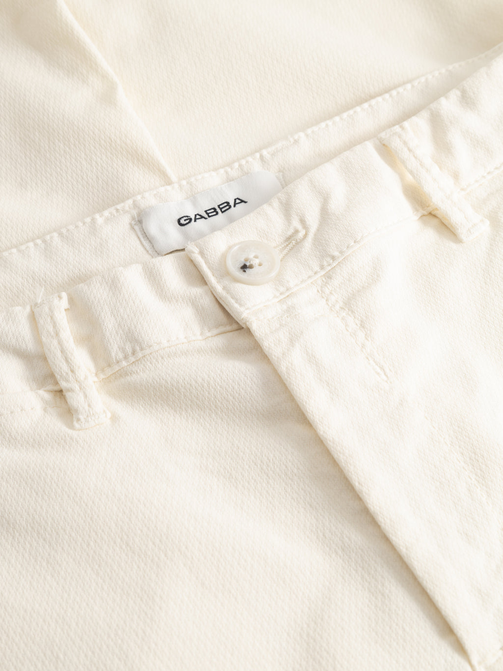 Close-up of the waistband and button on the Gabba GABpaul K3280 Dale Chino - White, featuring visible stitching, belt loops, French pockets, and an inner fabric label reading 