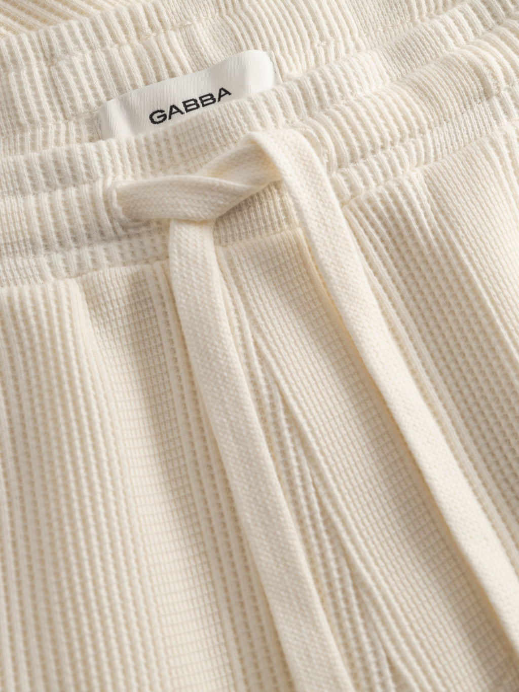 Close-up of GABtommi Wup Shorts in bone white by Gabba, featuring a ribbed knit design, comfortable waistband with drawstring, and a white label reading 