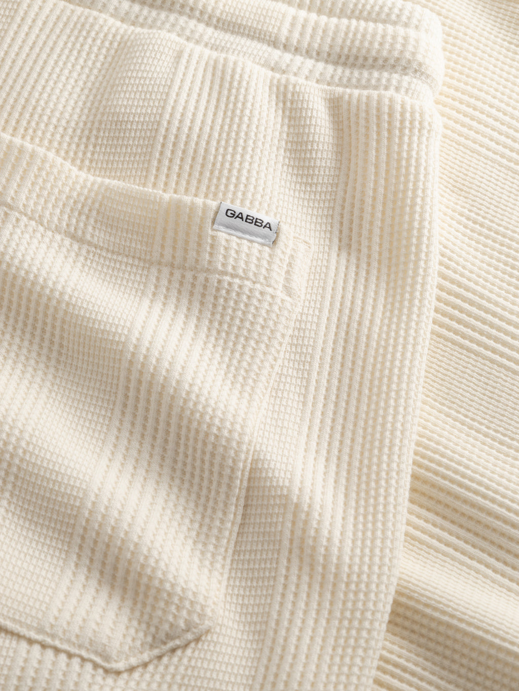 Close-up of the Gabba GABtommi Wup Shorts in Bone White, featuring textured cream-colored fabric with vertical ribbing and a small white label reading 