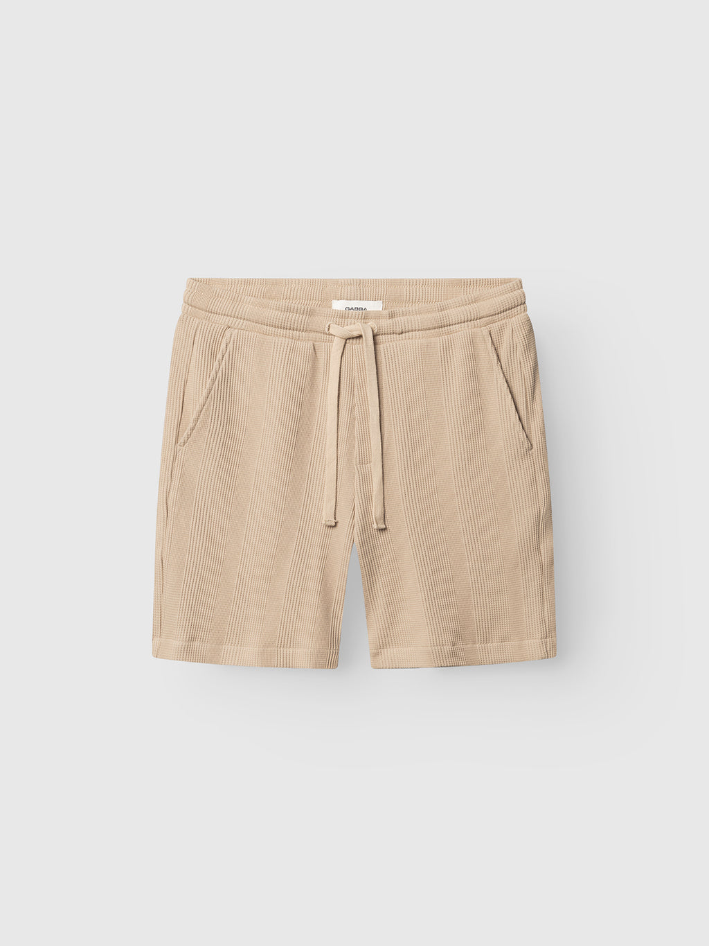 The Gabba GABtommi Wup Shorts in Humus feature a beige ribbed knit design, adjustable waistband with drawstring tie, and two side pockets, shown flat on a light gray background.