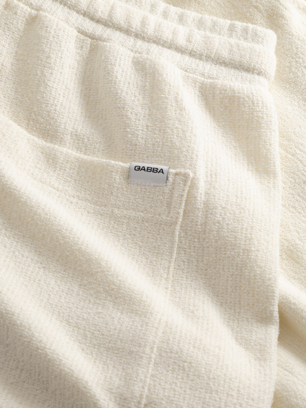 Close-up of Gabba GABtommi Towel Shorts in Egret, featuring cream-colored textured terry cotton, an elastic waistband, front pocket, and a small white 