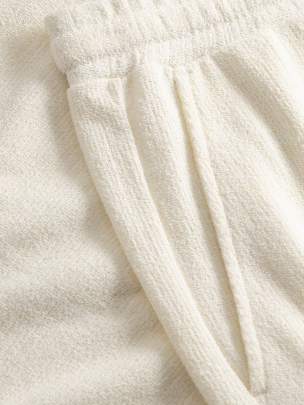 Close-up of Gabba GABtommi Towel Shorts in Egret, featuring cream-colored textured terry cotton, an elastic waistband, and a visible side pocket.