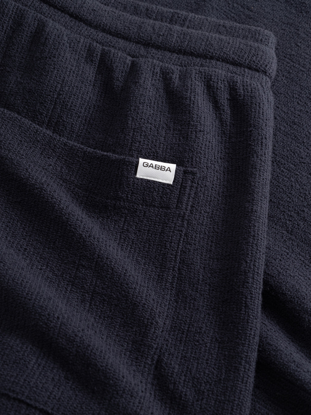Close-up of GABtommi Towel Shorts in navy terry cotton, featuring an elastic waistband, front pocket, and a small white Gabba label sewn on the pocket.