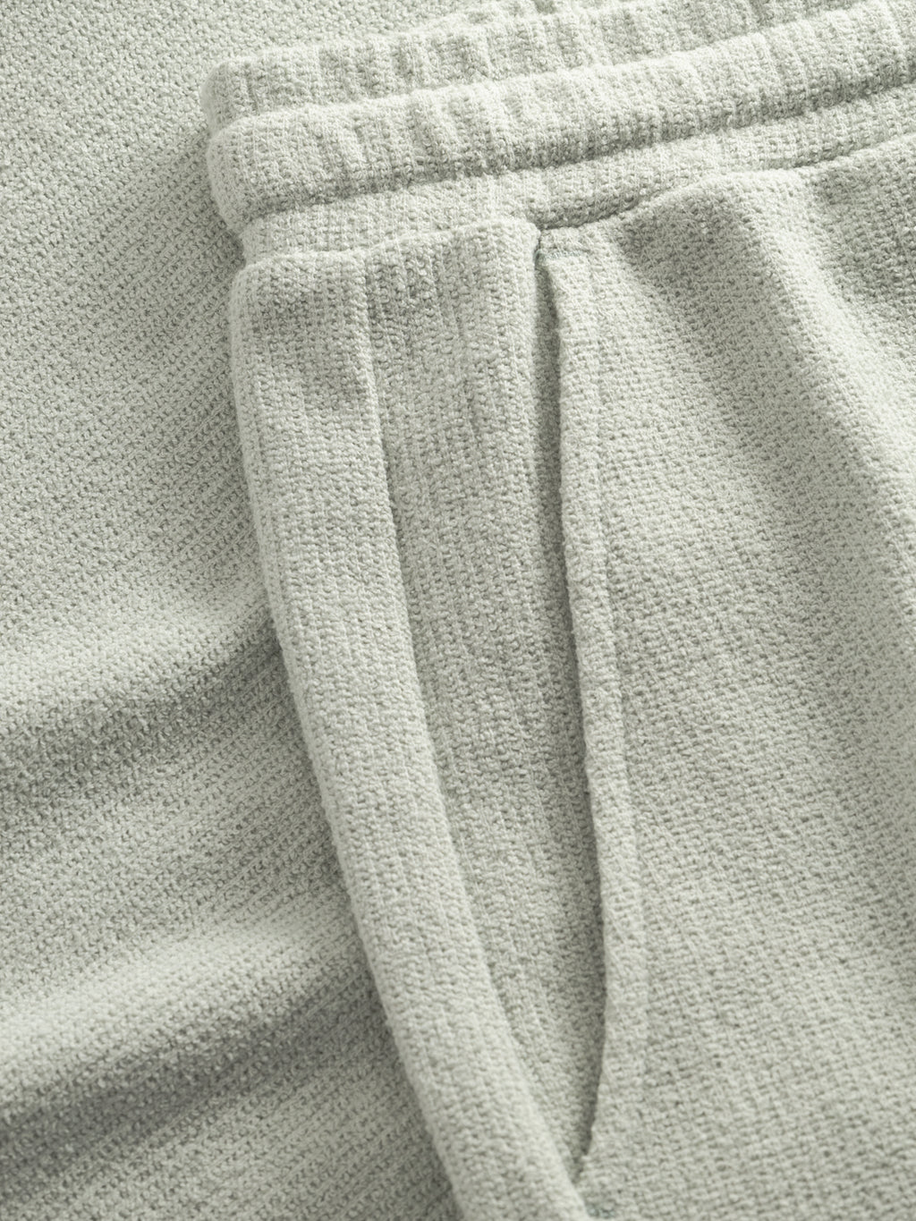 Close-up of Gabba GABtommi Towel Shorts in Mineral Gray, featuring an elastic waistband and a side pocket, laid flat on a matching surface.