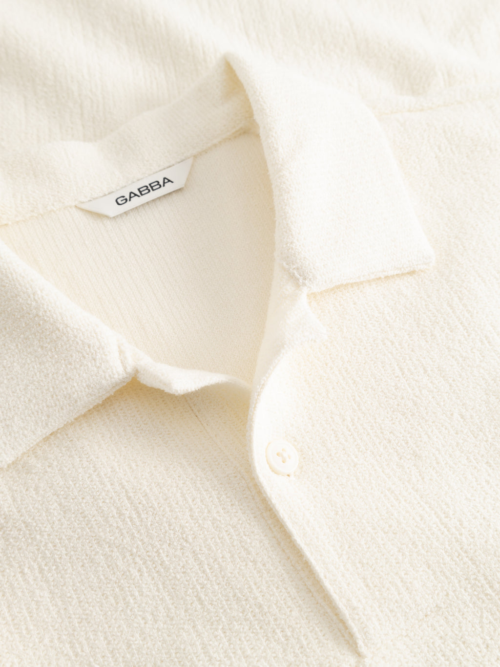 Close-up of the Gabba GABlio Sku Towel T-Shirt in Egret, showcasing its off-white textured fabric, polo collar with buttons, and a visible Gabba logo label inside the neckline.