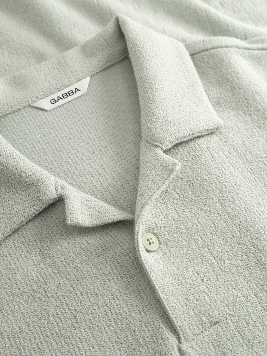 Close-up of the Gabba GABlio Sku Towel T-Shirt in Mineral Gray, featuring textured terry cotton, a polo collar with two buttons, and an inner neckline label displaying the Gabba logo.