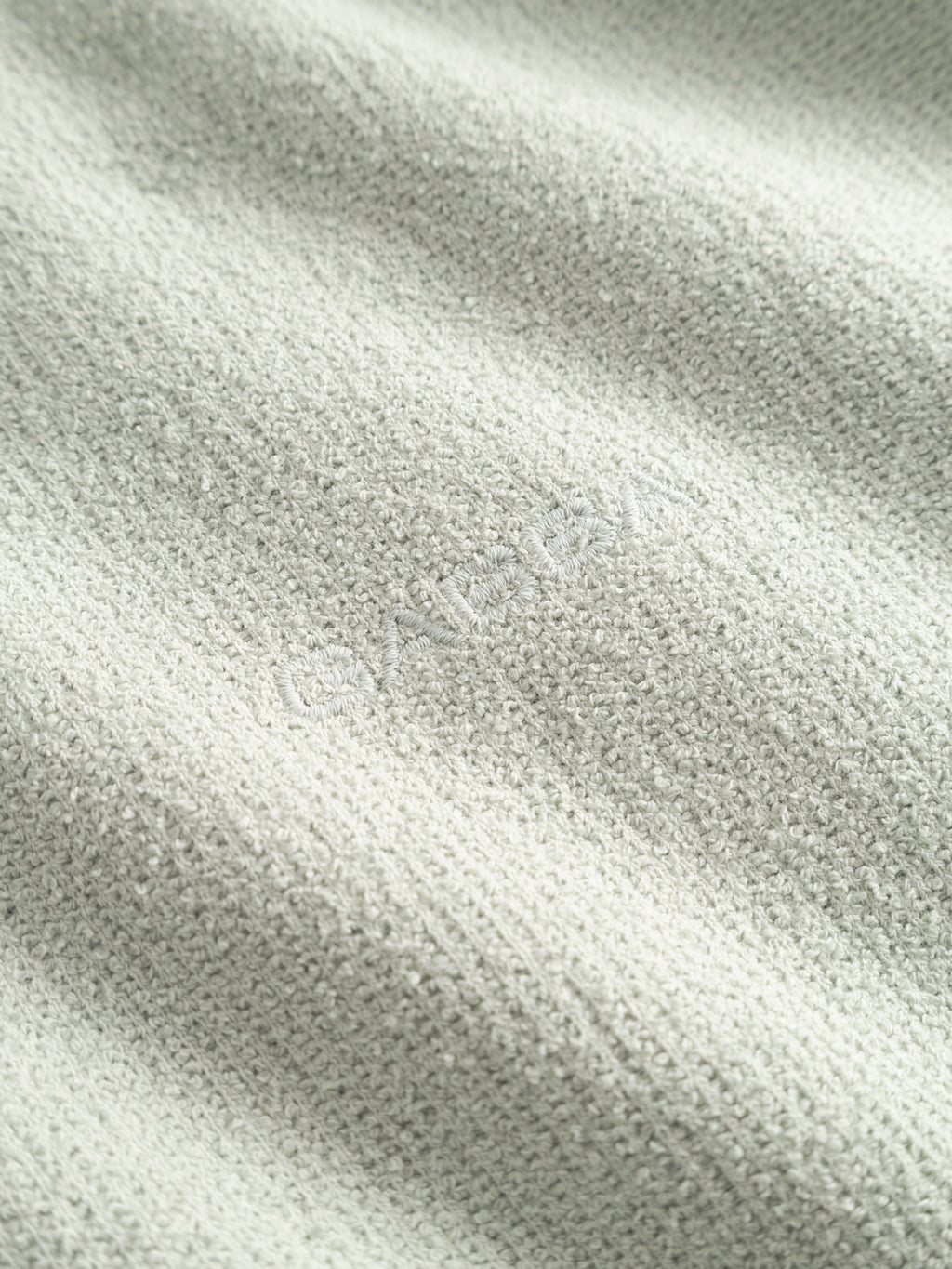 Close-up of the Gabba GABlio Sku Towel T-Shirt in Mineral Gray, featuring subtle terry cotton texture and soft folds. The word ISADORA is faintly embroidered in matching gray, blending seamlessly with the fabric.