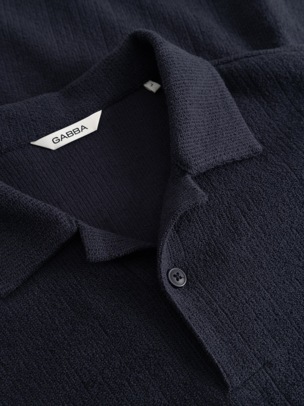 A close-up of the GABlio Sku Towel T-Shirt - Night Sky by Gabba shows its textured dark navy terry cotton blend, a single button, and a white 