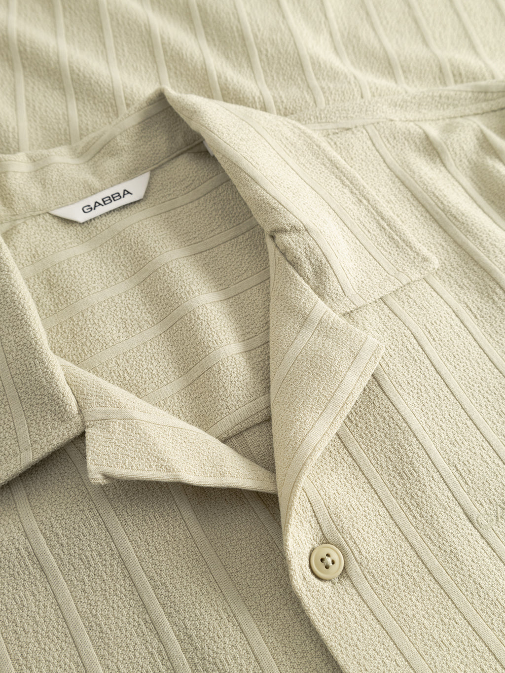 Close-up of the GABvalente Armor SS T-Shirt in Alfa Green by Gabba, featuring a resort collar, vertical stripes, a button, textured cotton-blend fabric, and a visible white Gabba label.
