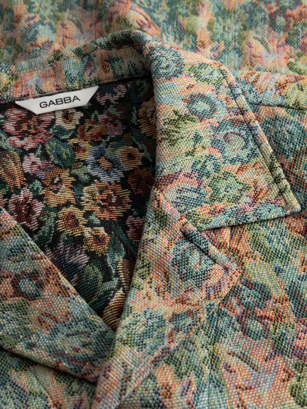 Close-up of Gabba's GABaustin POKT Kscope LS Overshirt—an abstract floral overshirt in green, yellow, pink, and orange tones with textured fabric. A white 