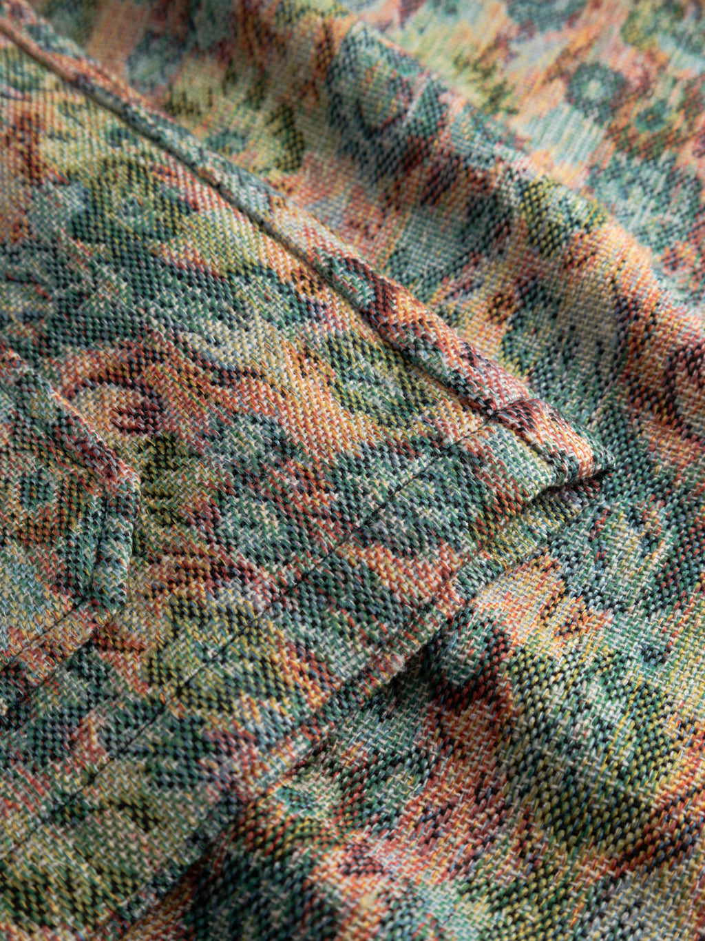 Close-up of textured fabric from the Gabba GABaustin POKT Kscope LS Overshirt - Abstract Flowers, featuring a vibrant floral pattern in green, orange, yellow, and blue. Highlights the weave and overlapping edges of this stylish layering piece.