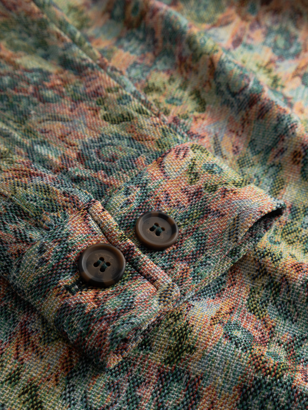 Close-up of Gabba's GABaustin POKT Kscope LS Overshirt - Abstract Flowers, showing textured fabric with a colorful floral pattern and two brown buttons on the cuff—ideal as an eye-catching layering piece.