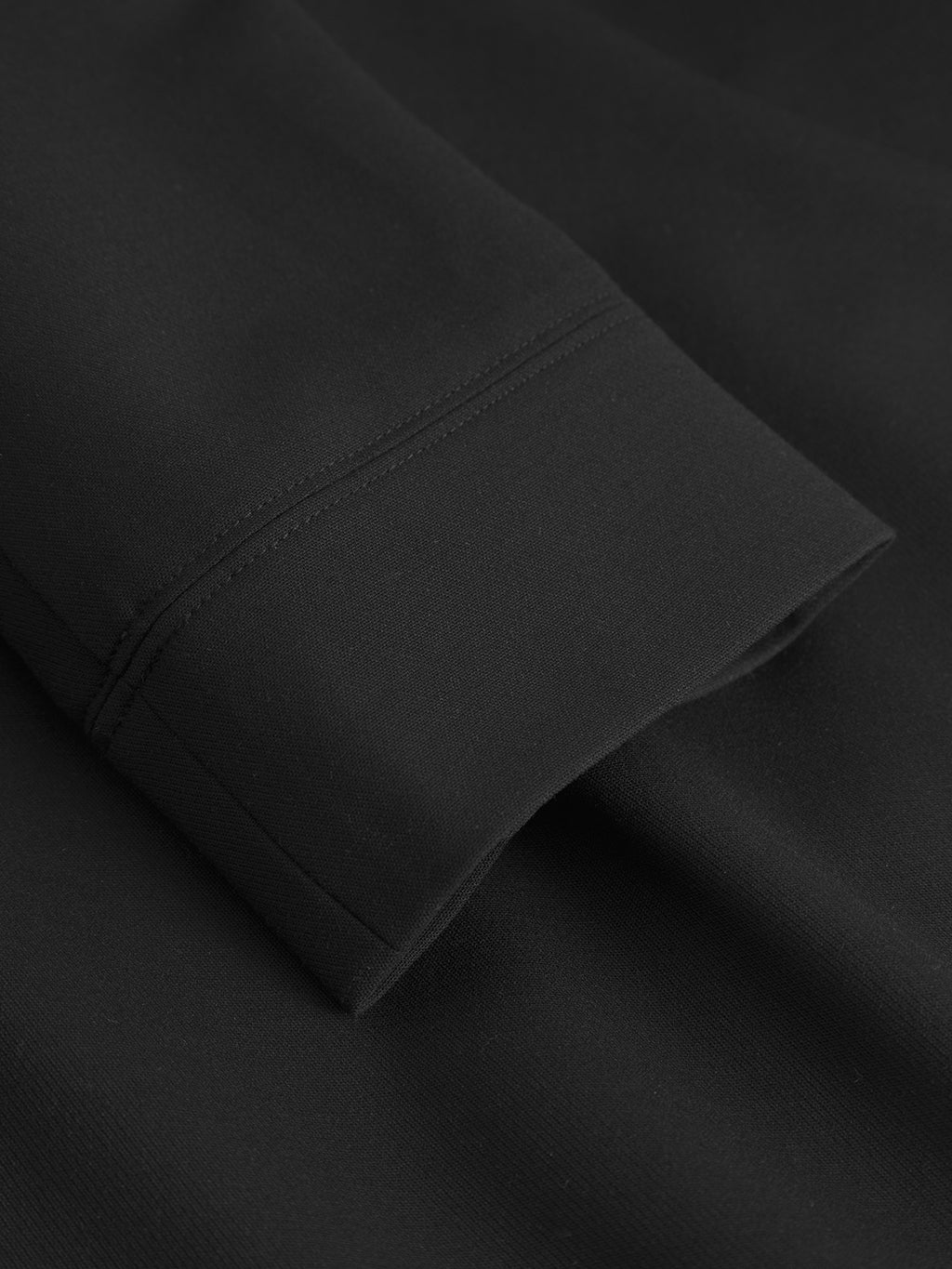 A close-up of the Gabba GABnik Phin GRS - Black jacket’s sleeve, showing its neat double-stitched seams as it rests on matching black fabric.