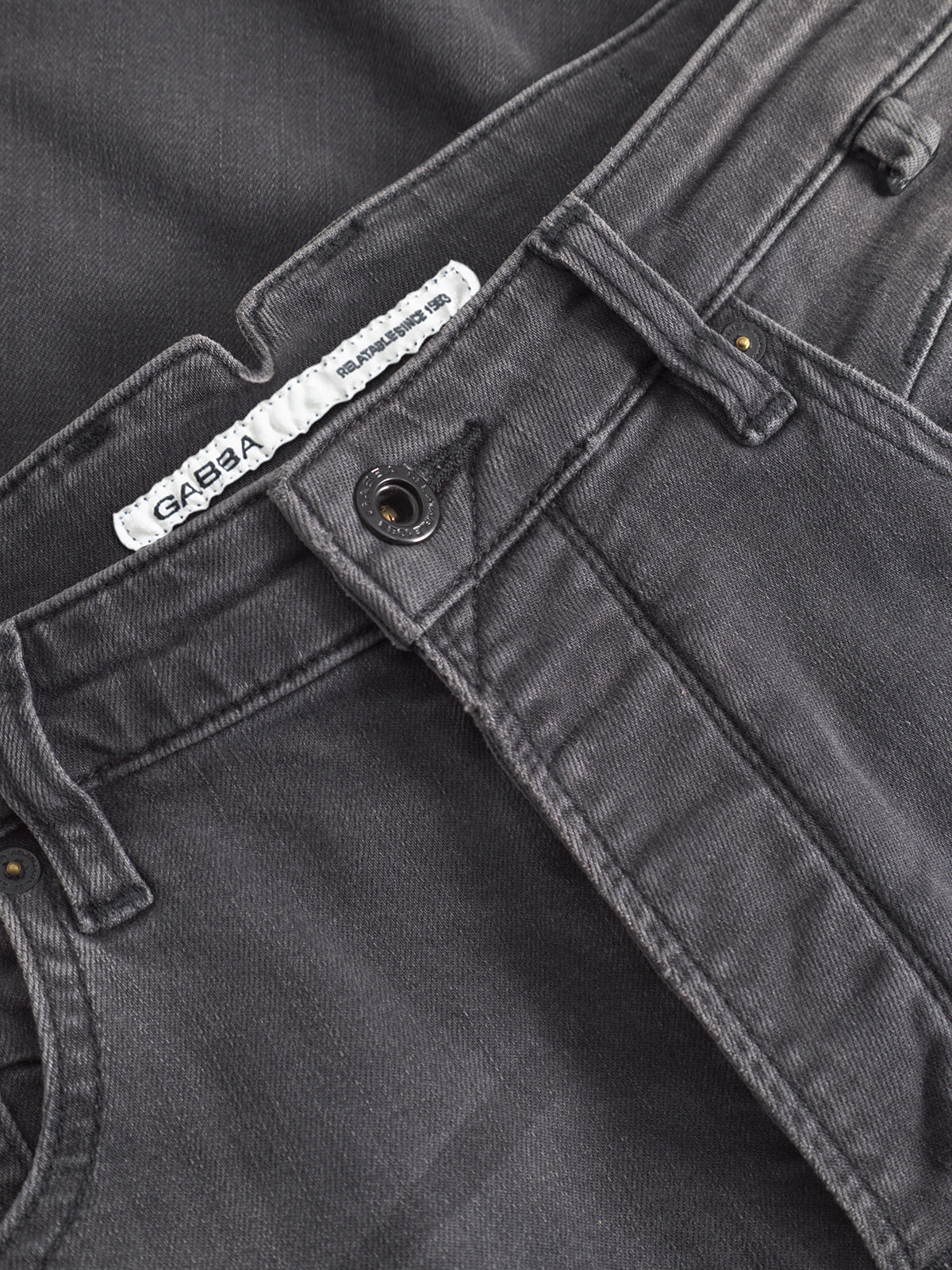 Close-up of the waistband and front button of GABBA's GABalex Thor Cropped Jeans - Denim wash, showcasing worker cut waistbands, belt loops, neat stitching, and a white brand label for a fashion-forward fit.