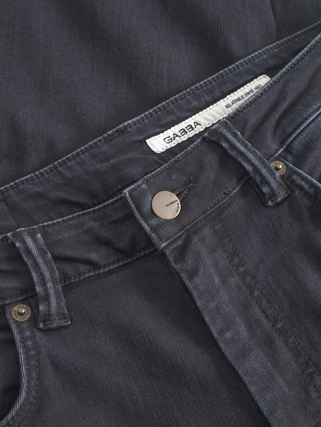 Close-up of the waistband and button on GABjones BlueBlack denim jeans by Gabba, featuring a white inner brand label. These dark blue jeans offer all-day comfort due to their high flexibility.