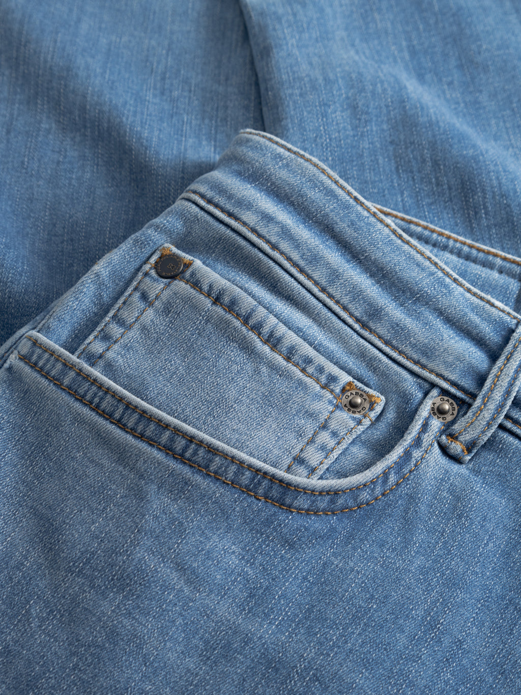 Close-up of the GABjones Dhera Jeans by Gabba in light blue denim, highlighting the front pocket area with distinct stitching and metal rivets. The fabric texture and seams of these slim straight fit jeans are clearly showcased.