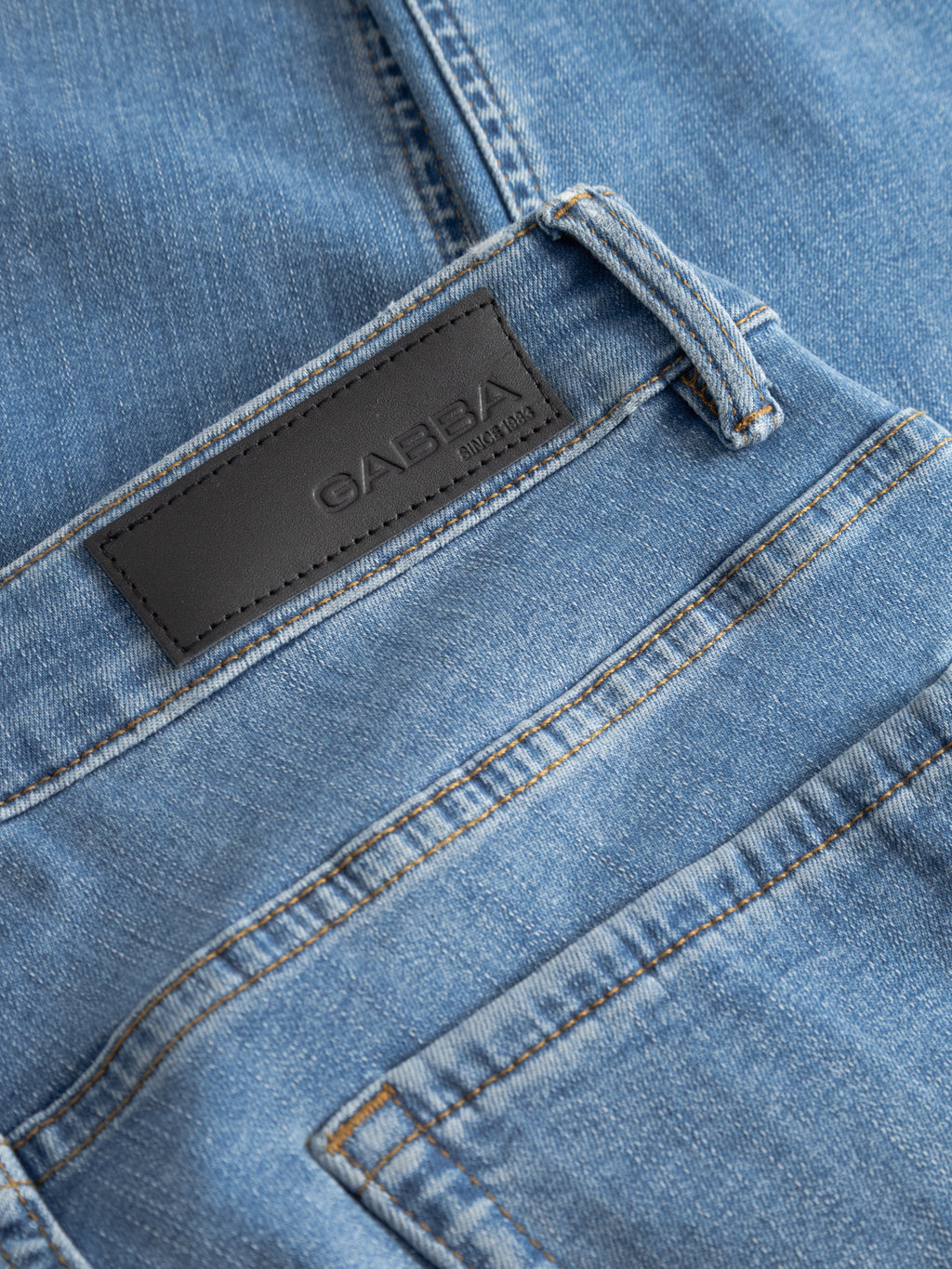 Close-up of the GABjones Dhera Jeans in light blue denim by Gabba, featuring a black leather Gabba patch, belt loop, and part of the back pocket with yellow stitching, crafted from superstretch denim in a slim straight fit.