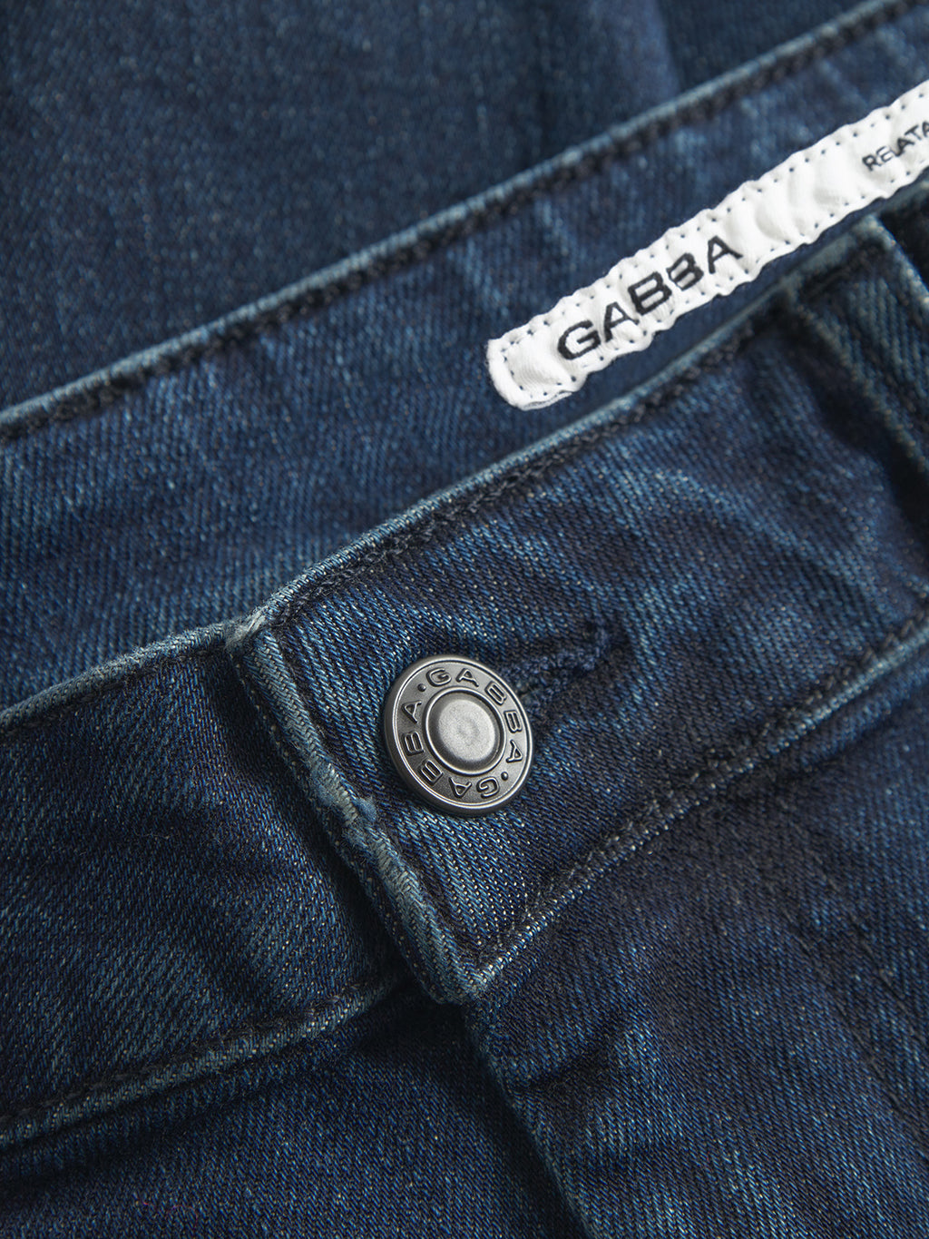 Close-up of GABmarc Mego - Dark Blue Denim jeans by Gabba, featuring a metal button and a white fabric label on the waistband, both branded with Gabba, crafted using Wiser Wash technology.