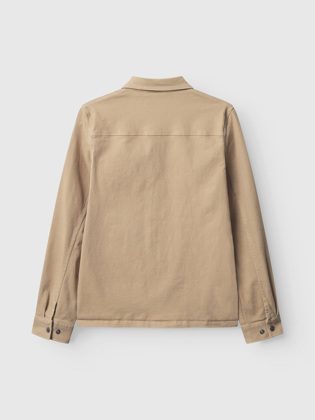 The Gabba GABbeta Twill - Sand overshirt is shown from the back, laid flat on a white background. This beige, long-sleeve workwear shirt features a collar, buttoned cuffs, and a clean, minimalist design.