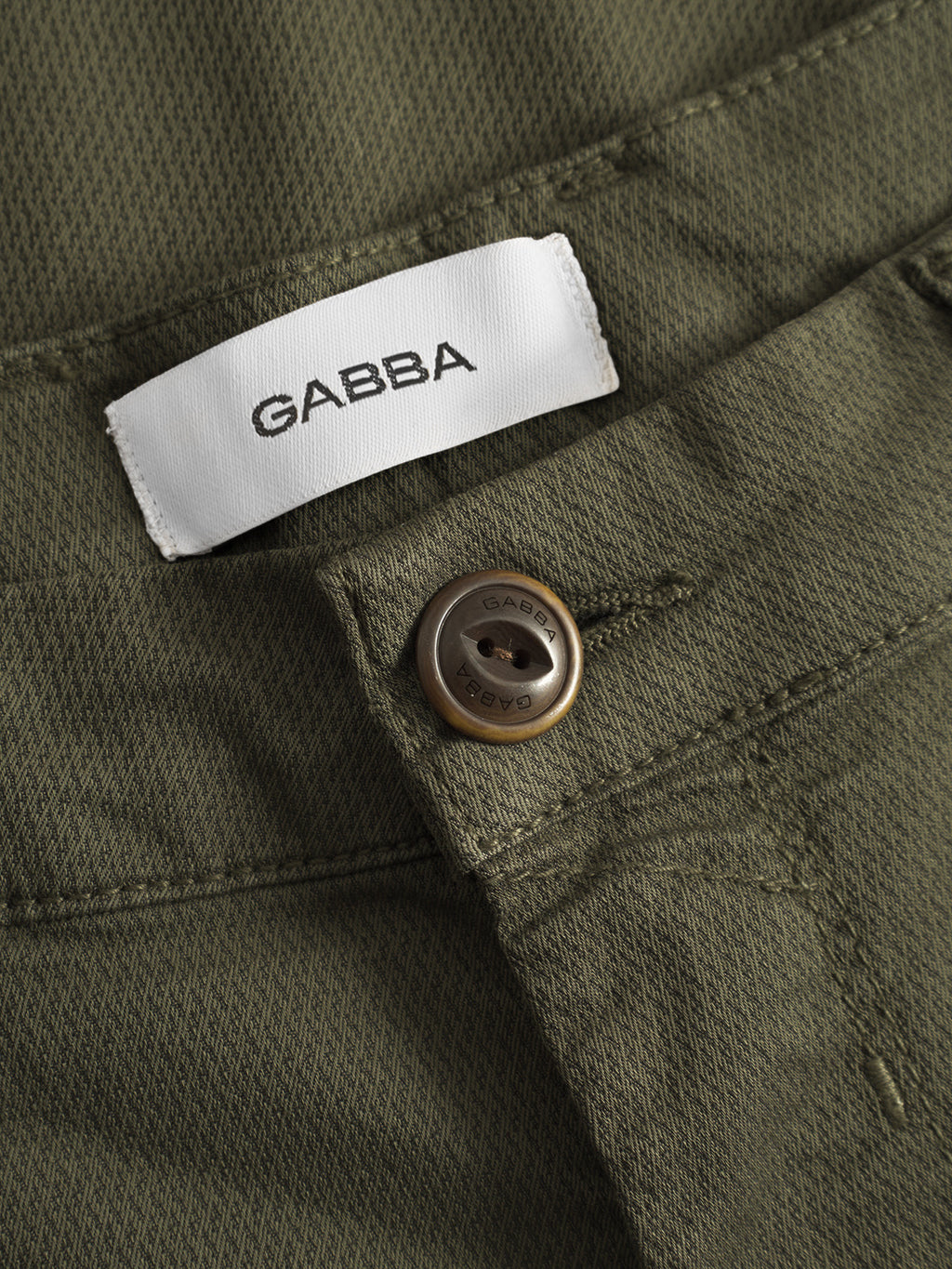 Close-up of the GABBA GABpaul K3280 Dale Chino in Army, featuring French pockets, a white GABBA label, and a metal button engraved with the brand name. The fabric texture and classic stitching details are clearly visible.