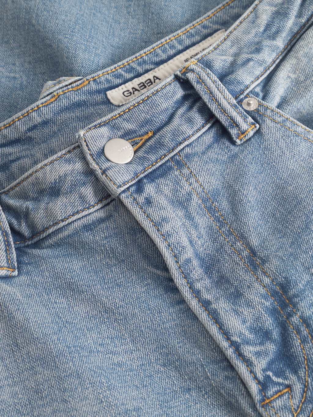 Close-up of Gabba GABcarl CrosV2 Jeans in light blue denim, showing a metal button, belt loop, detailed stitching, and the GABBA label inside the waistband.
