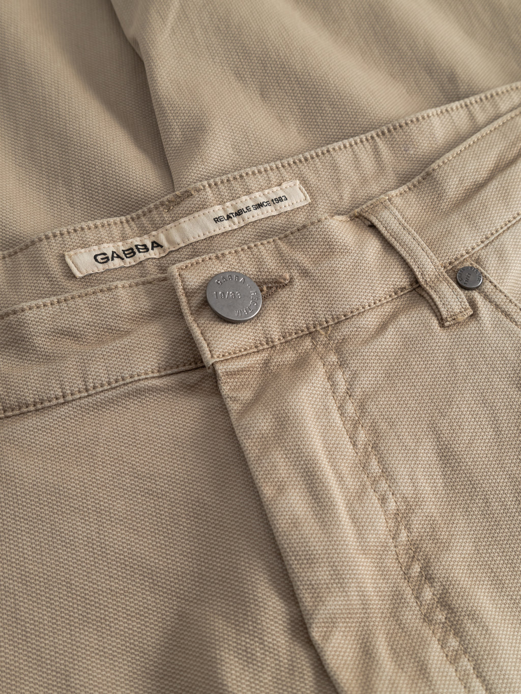 Close-up of Gabba GABmarc 5poc Marlo - Coriander jeans in beige, showing visible stitching, a metal button, and a white label with Gabba branding on the textured waistband, emphasizing comfort and style.