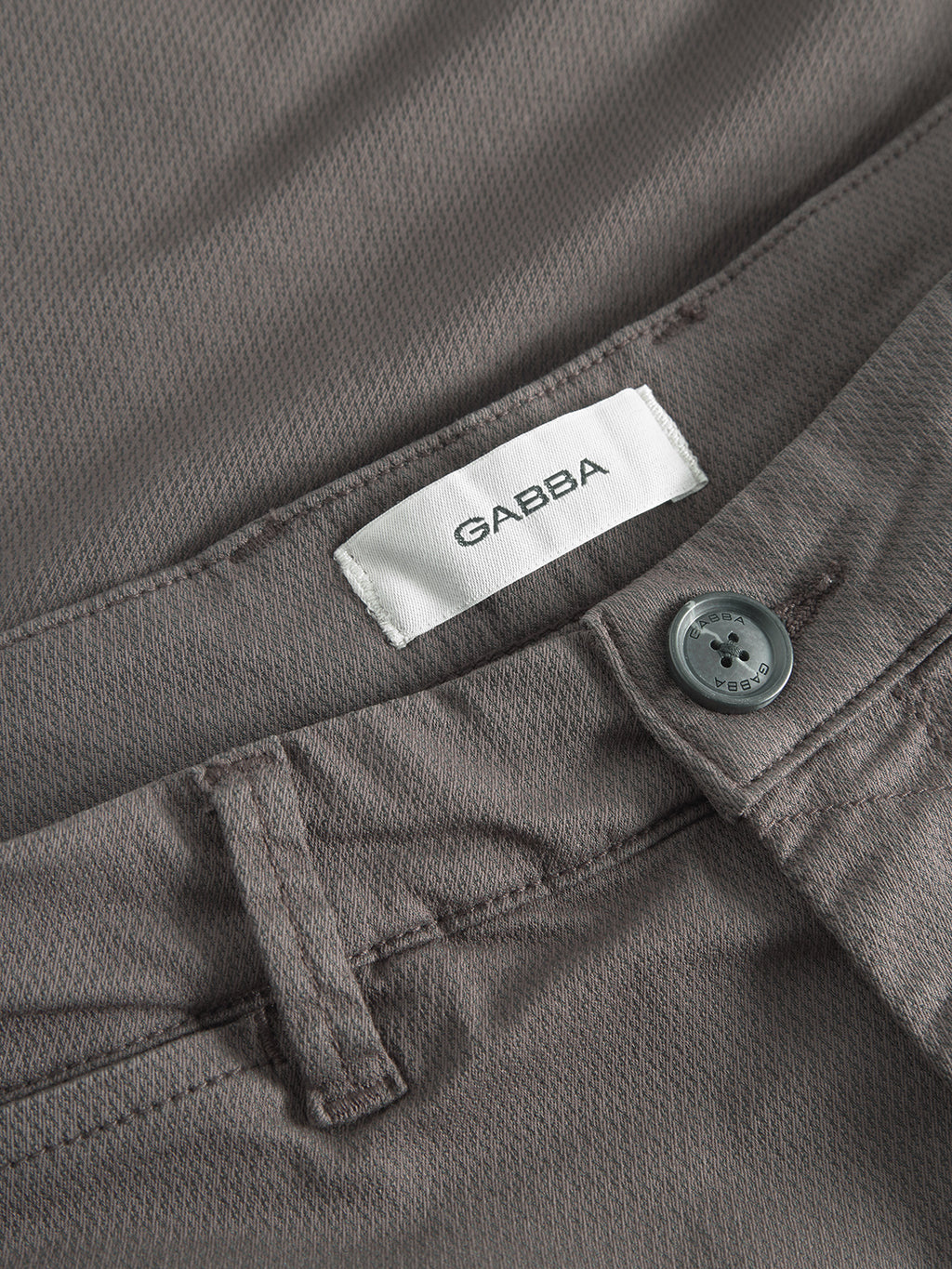 Close-up of Gabba GABpaul K3280 Dale Chino in charcoal, highlighting the waistband with a white Gabba label, belt loop, French pockets, and gray button above the zipper.