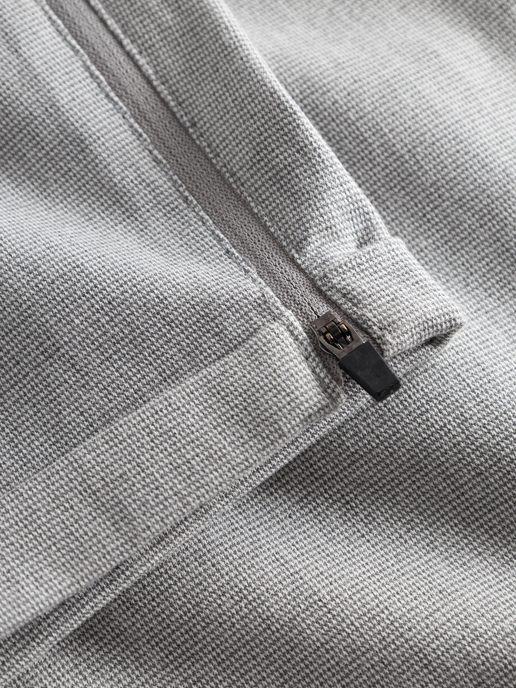Close-up of Gabba Pisa Domo Pants in Monument: detailed view of the light gray textured fabric and partially unzipped zipper, highlighting stitching, material, and zipper pull in sharp focus.