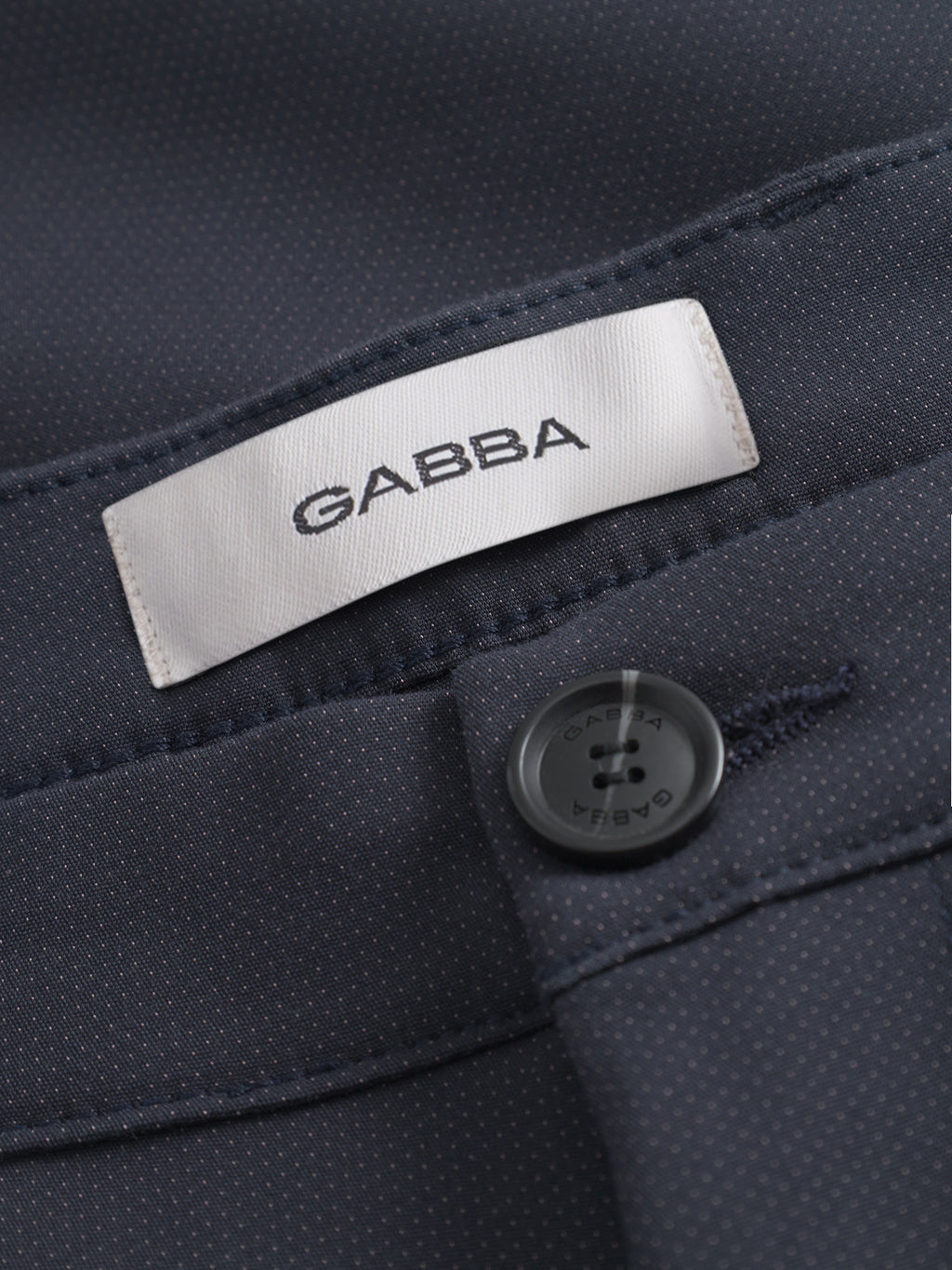 Close-up of GABBA Pisa Small Dot - Navy pants, made from high-stretch cotton-blend fabric with a refined dotted texture. Features a white GABBA label and dark button for sharp metro style detailing.