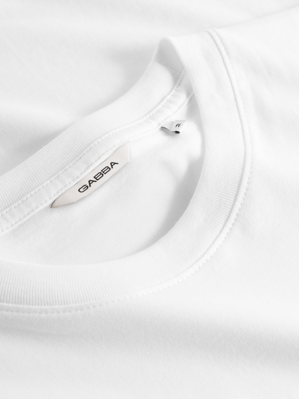 Close-up of a folded white Gabba GABdune Logo GOTS SS T-Shirt with visible neckline and tag, showcasing the smooth fabric and classic timeless style.