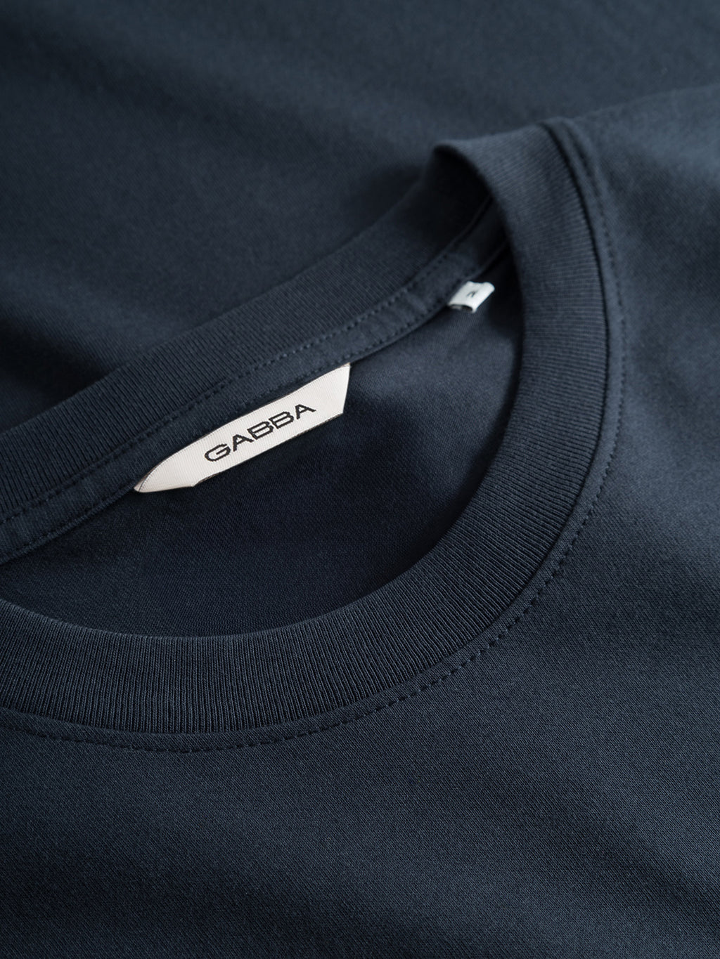 Close-up of the Gabba GABdune Logo GOTS SS T-Shirt in Total Eclipse, featuring a visible white Gabba label inside the collar and smooth, neatly stitched fabric that highlights its premium, GOTS-certified quality.