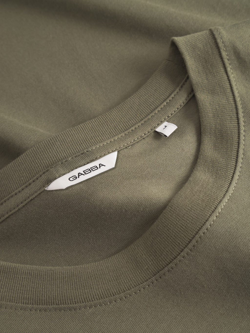 Close-up of the Gabba GABdune Logo GOTS SS T-Shirt in Deep Lichen Green, classic fit with a round neckline, showing a white Gabba label and an L size tag.