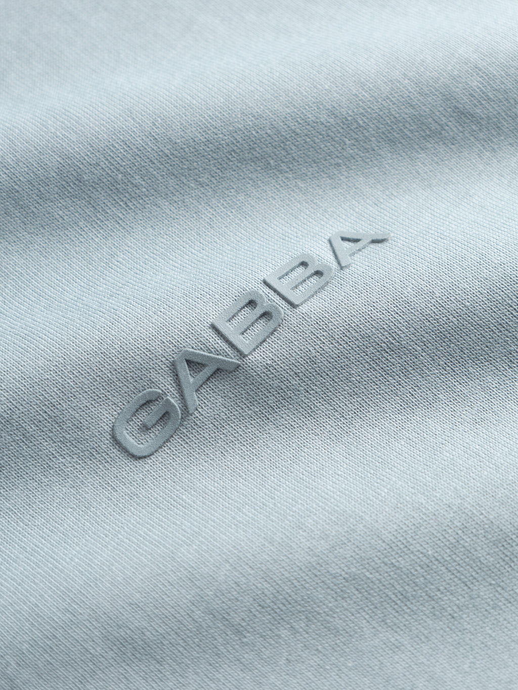 Close-up of light blue organic cotton GABdune Logo GOTS SS T-Shirt fabric by Gabba, featuring the brand name embossed in a matching shade.