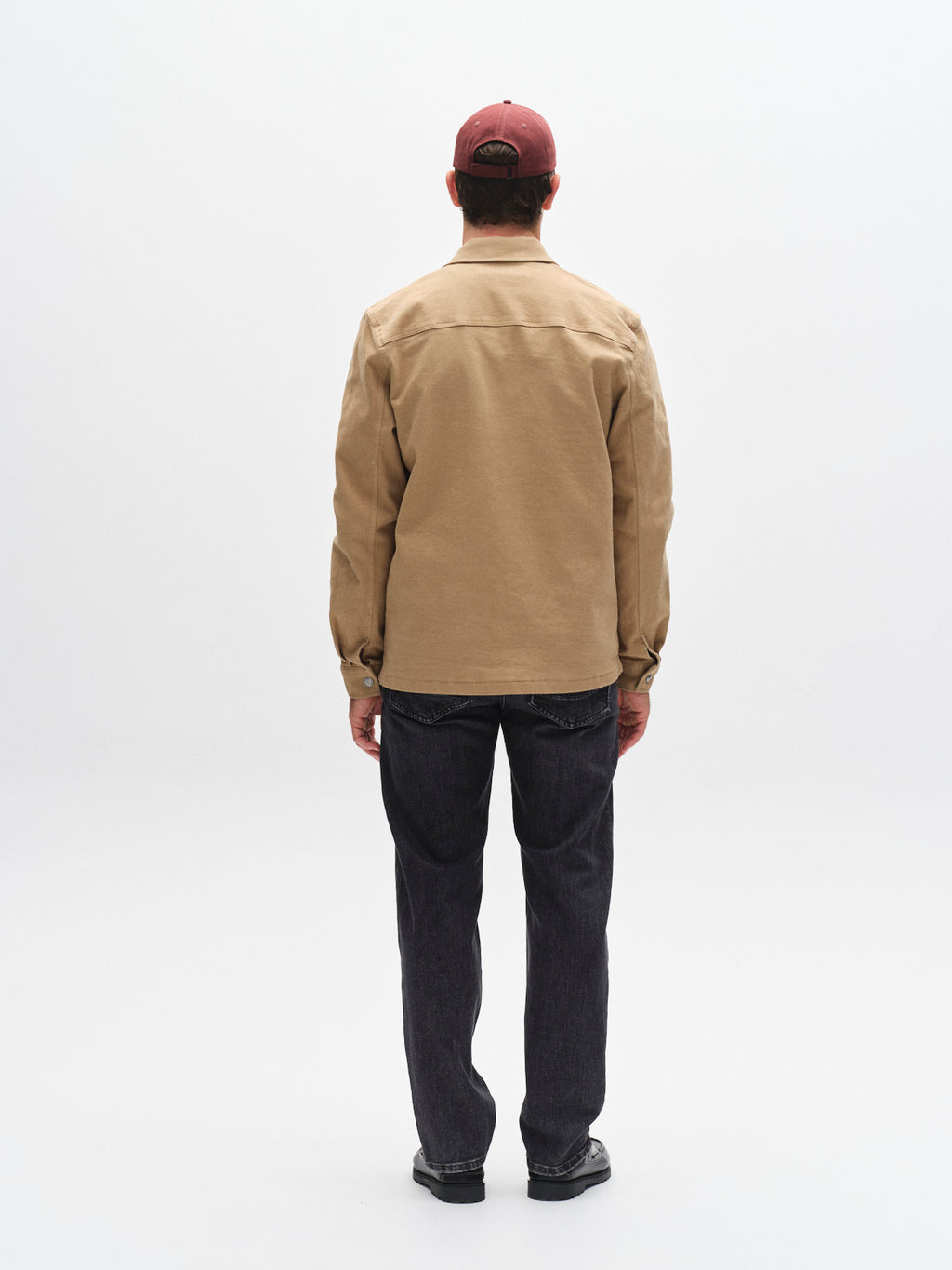 A person faces away from the camera, wearing a tan jacket, black shoes, a red baseball cap, and Gabba’s GABmax F1011 - Black Denim jeans against a plain white background.