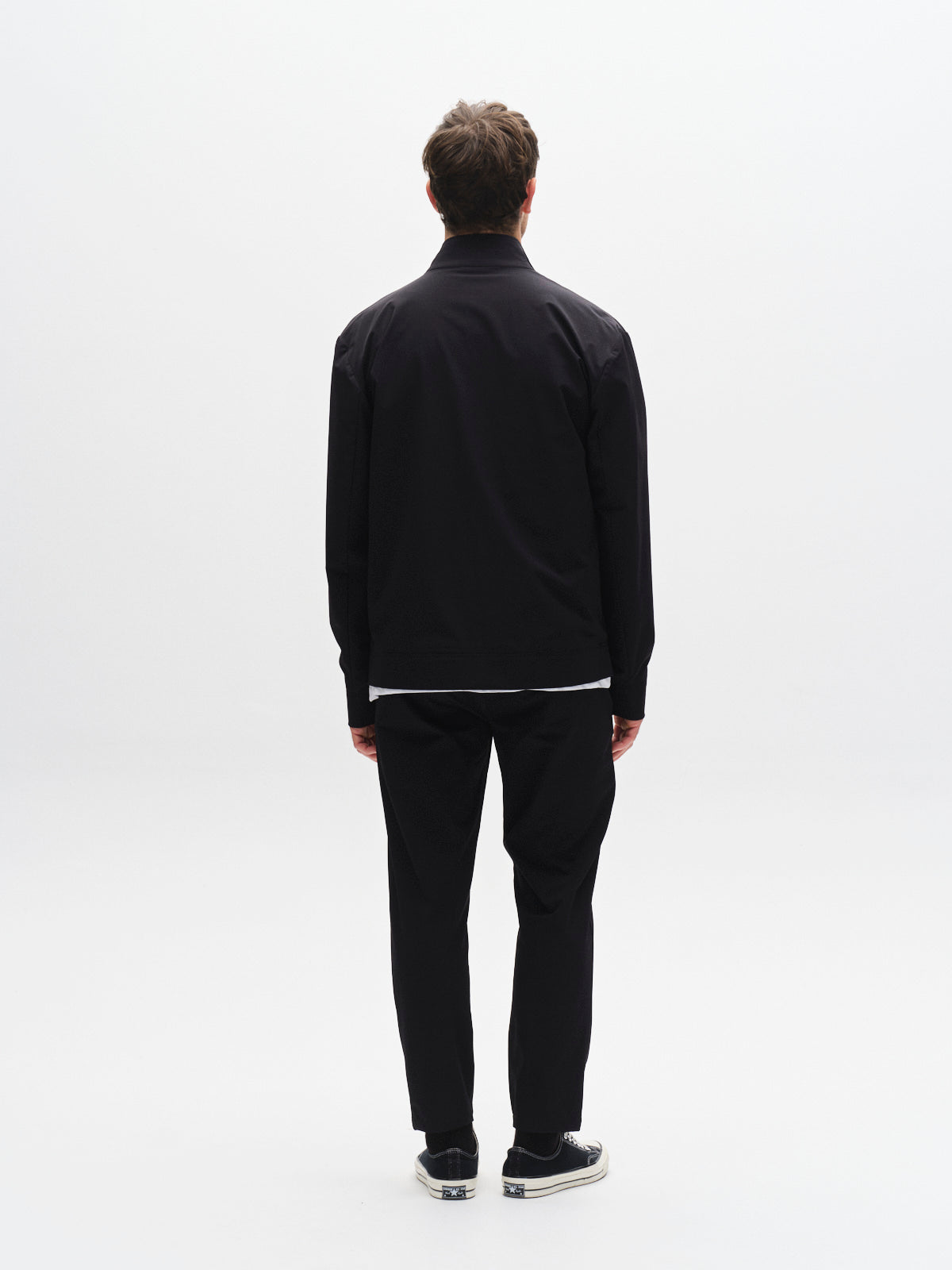 A man faces away from the camera in a Gabba GABnik Tech - Black jacket, paired with black pants and black sneakers with white soles, set against a plain white background.