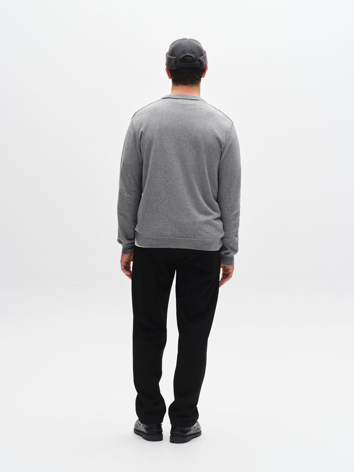 A person wearing a gray sweater, gray cap, and Gabba GABnapoli 19 Phin GRS - Black pants stands facing away from the camera against a plain white background. The regular straight fit of the Gabba pants gives the outfit a classic and polished appearance.