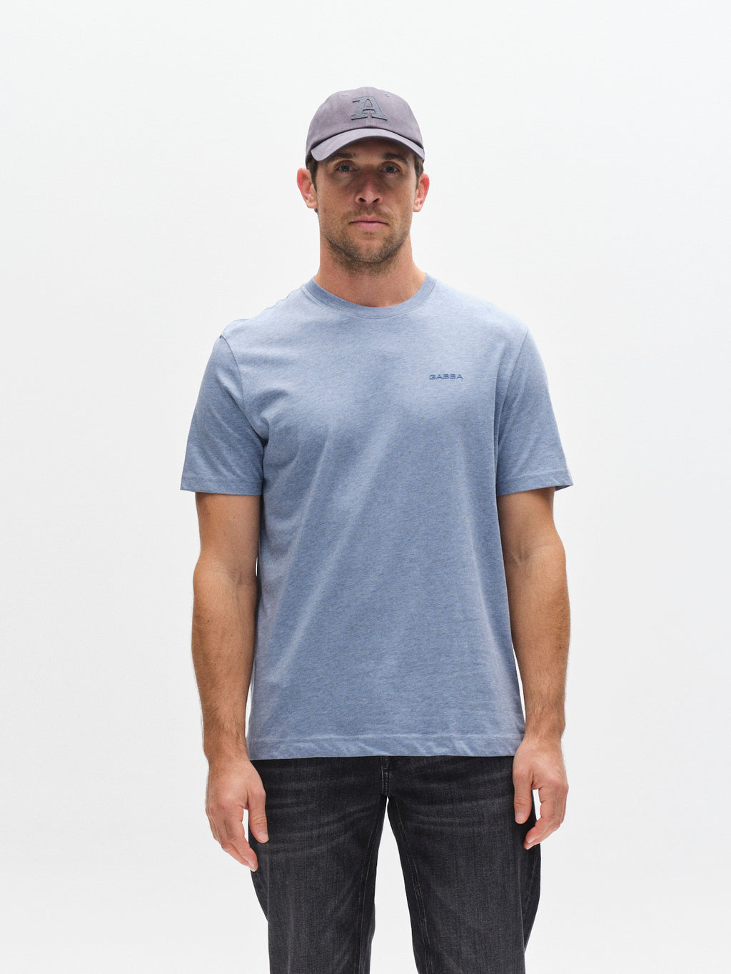 A man wearing the Gabba GABdune Melange New SS T-Shirt in Blue Melange, featuring a subtle chest logo, pairs it with dark jeans and a gray baseball cap as he stands facing forward against a plain white background. The soft melange jersey fabric of the T-shirt lends both comfort and style to his casual ensemble.