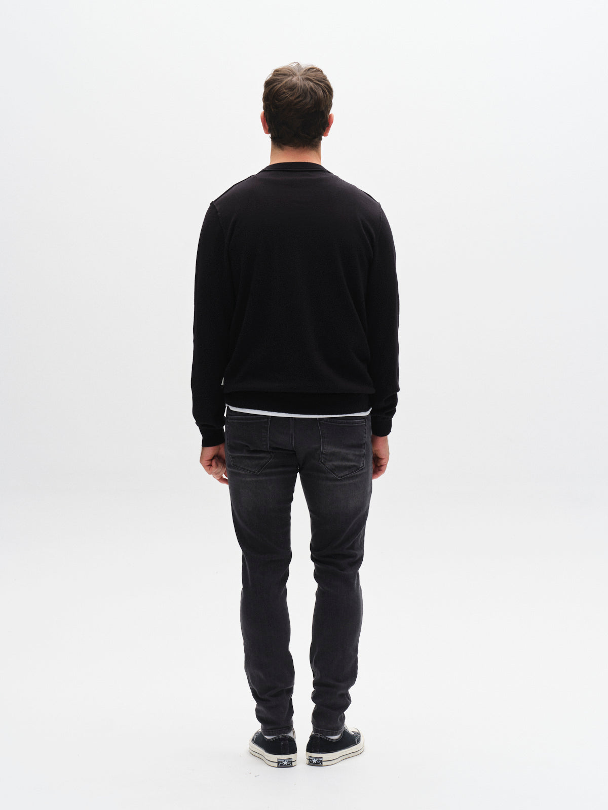 A man stands with his back to the camera against a plain white background, wearing GABBA’s GABrey Thor Jeans in denim wash and a black sweatshirt for a laid-back look.