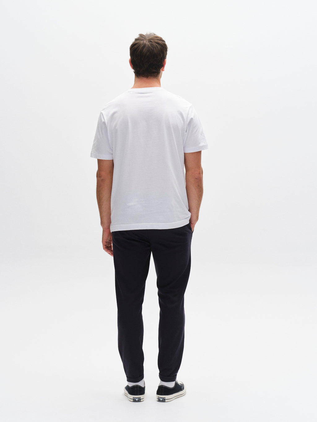 A man faces away from the camera in a plain white t-shirt, black slip-on shoes, and GABBA Pisa Small Dot - Navy pants against a white background, highlighting metro style and high-stretch cotton-blend comfort.