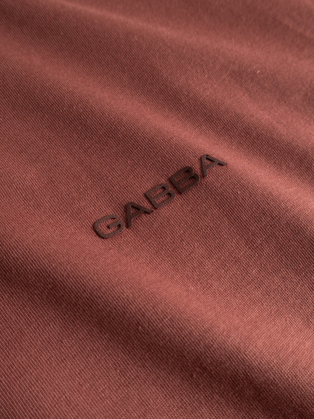 Close-up of the Gabba GABdune Logo GOTS SS T-Shirt in Brick Red, featuring the word “Gabba” embroidered in matching thread at the center.